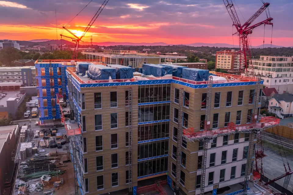 Aerial view of large building under construction with cranes against sunset sky in downtown Charlotteville, Virginia.